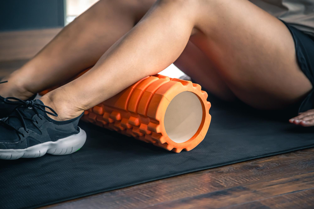 Person using an orange foam roller on their calves while seated on a mat, performing self-myofascial release for muscle recovery after their workout. 